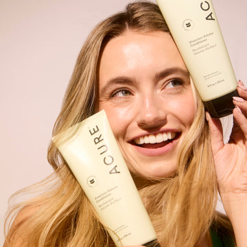 Woman smiling holding acure products on a nautral background